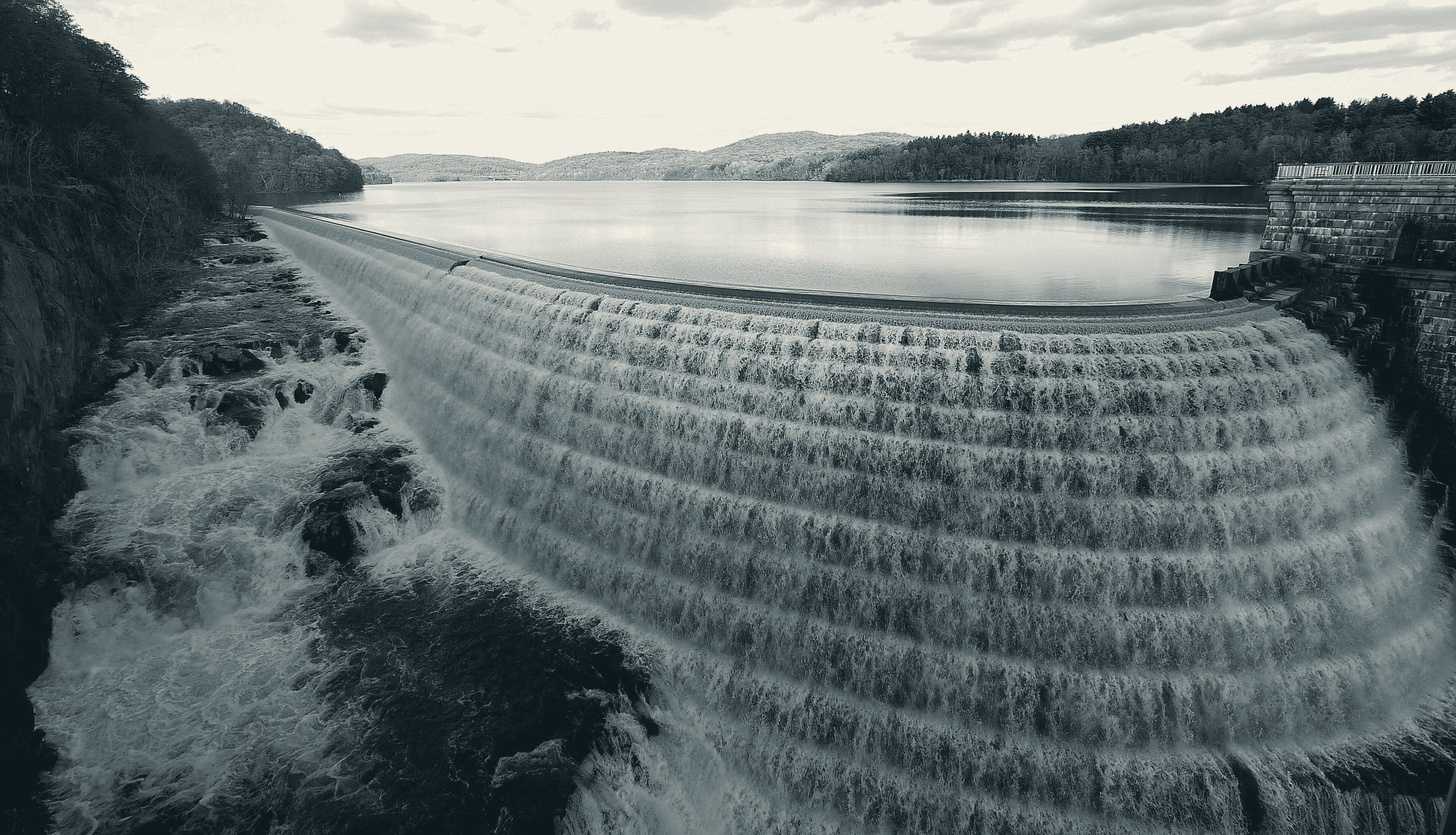 Water pouring over the stepped stone spillway of the New Croton Dam, with the reservoir behind it.